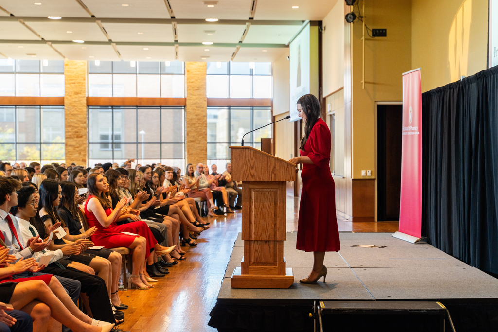 Photo by Paulius Musteikis PharmD student Jennifer Velikodanov speaks at the podium in front of the applauding class.