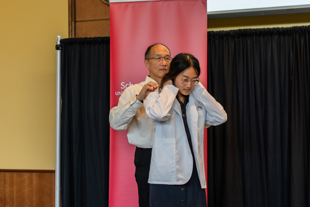 Photo by Paulius Musteikis A student receives her white coat from an older man