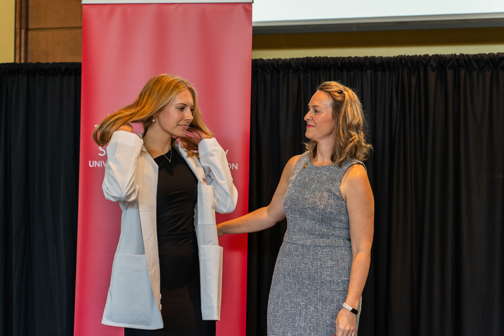 2024 White Coat Ceremony A female student adjusts her hair after receiving her white coat from Kate Rotzenberg