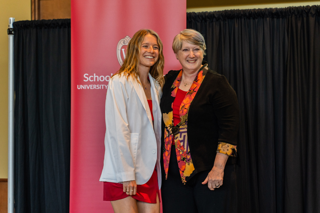 2024 White Coat Ceremony A student poses with Karen Kopacek in front of a red School of Pharmacy banner
