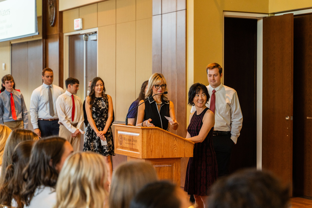Photo by Paulius Musteikis Faculty stand at a podium, students lined up behind them waiting for their white coats.