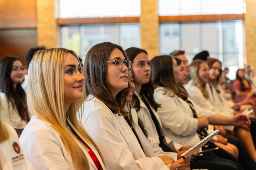 Photo by Paulius Musteikis Students in white coats smile and listen to a speaker