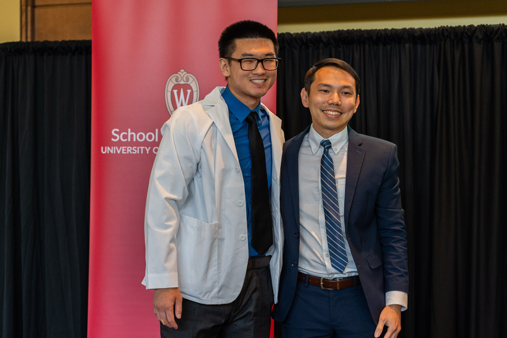 Photo by Paulius Musteikis A student in a white coat poses with Sean Lim in front of a red School of Pharmacy banner