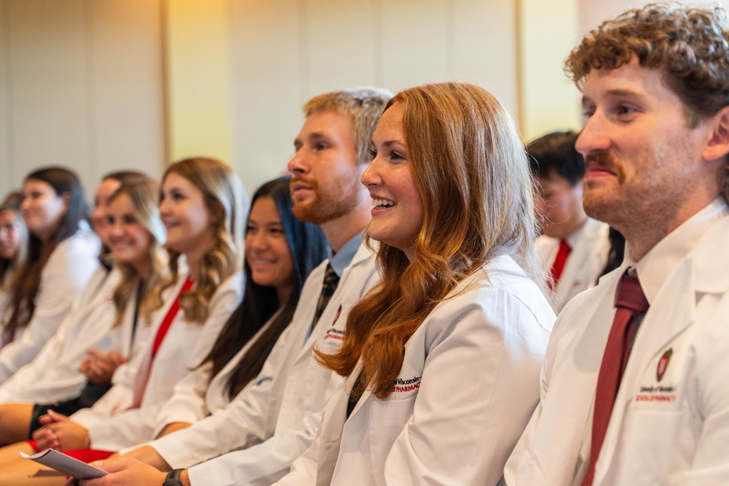 Photo by Paulius Musteikis Students in white coats smile and listen to a speaker