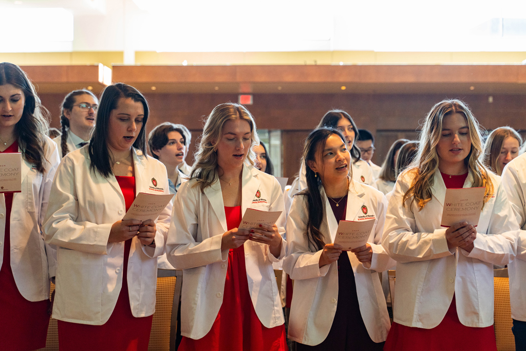 Photo by Paulius Musteikis Students in white coats read the Oath of a Pharmacist off the backs of their ceremony programs