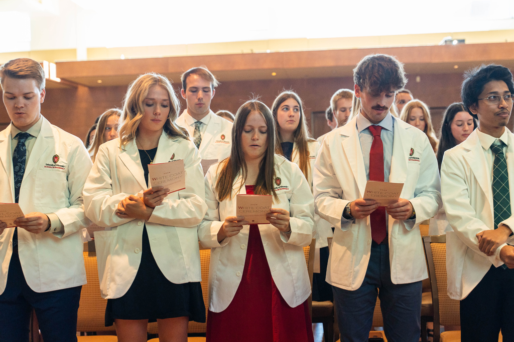 Photo by Paulius Musteikis Students in white coats read the Oath of a Pharmacist off the backs of their ceremony programs
