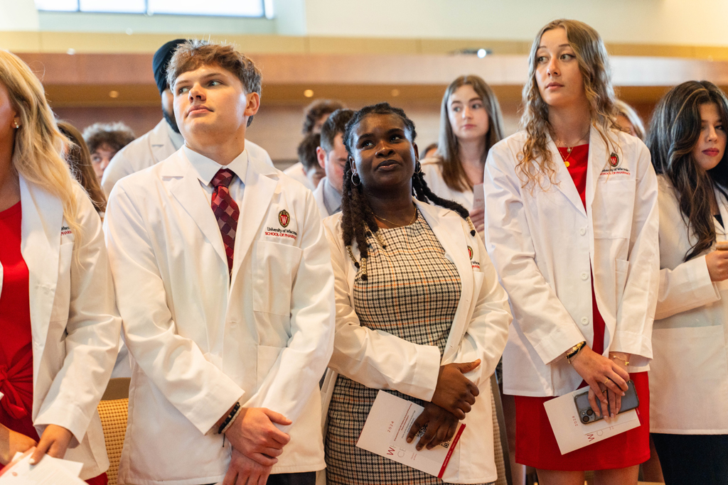 Photo by Paulius Musteikis Standing students in white coats listen in to a speaker
