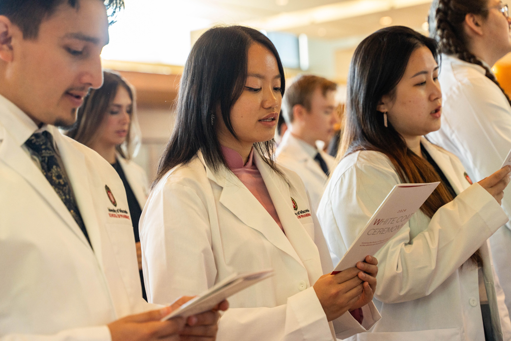 Photo by Paulius Musteikis Students in white coats read the Oath of a Pharmacist off of the backs of their White Coat Ceremony programs