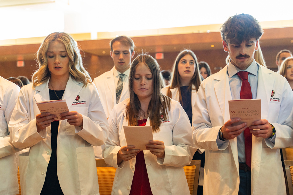 Photo by Paulius Musteikis Students in white coats read the Oath of a Pharmacist off of the backs of their White Coat Ceremony programs