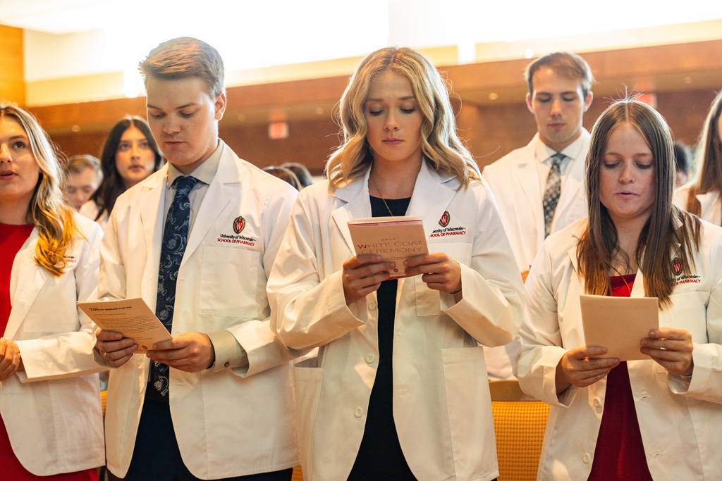 Photo by Paulius Musteikis Students in white coats read the Oath of a Pharmacist off of the backs of their White Coat Ceremony programs