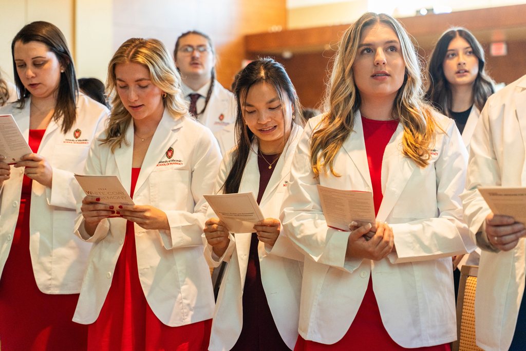 Photo by Paulius Musteikis Students in white coats read the Oath of a Pharmacist off of screens in front of the room