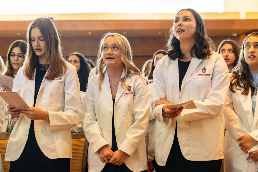 2024 White Coat Ceremony Students in white coats read the Oath of a Pharmacist off of screens in front of the room