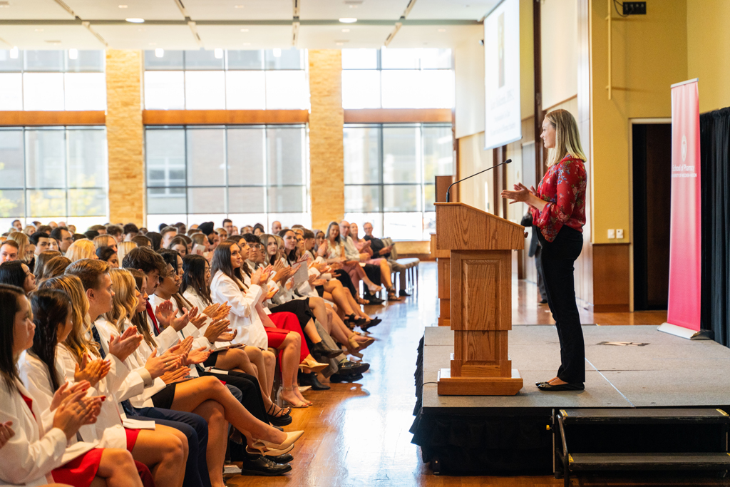 Photo by Paulius Musteikis Second-year PharmD student Katie Molkentin speaks at a podium to the Class of 2028 seated in chairs