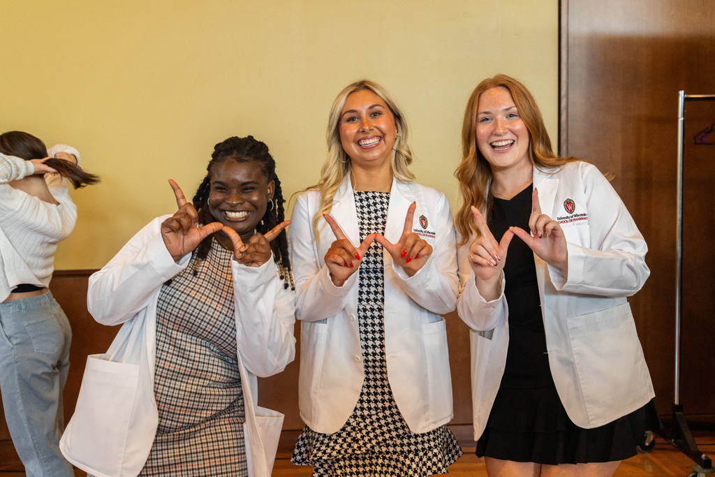 Photo by Paulius Musteikis Three female students in white coats hold up "W" hands