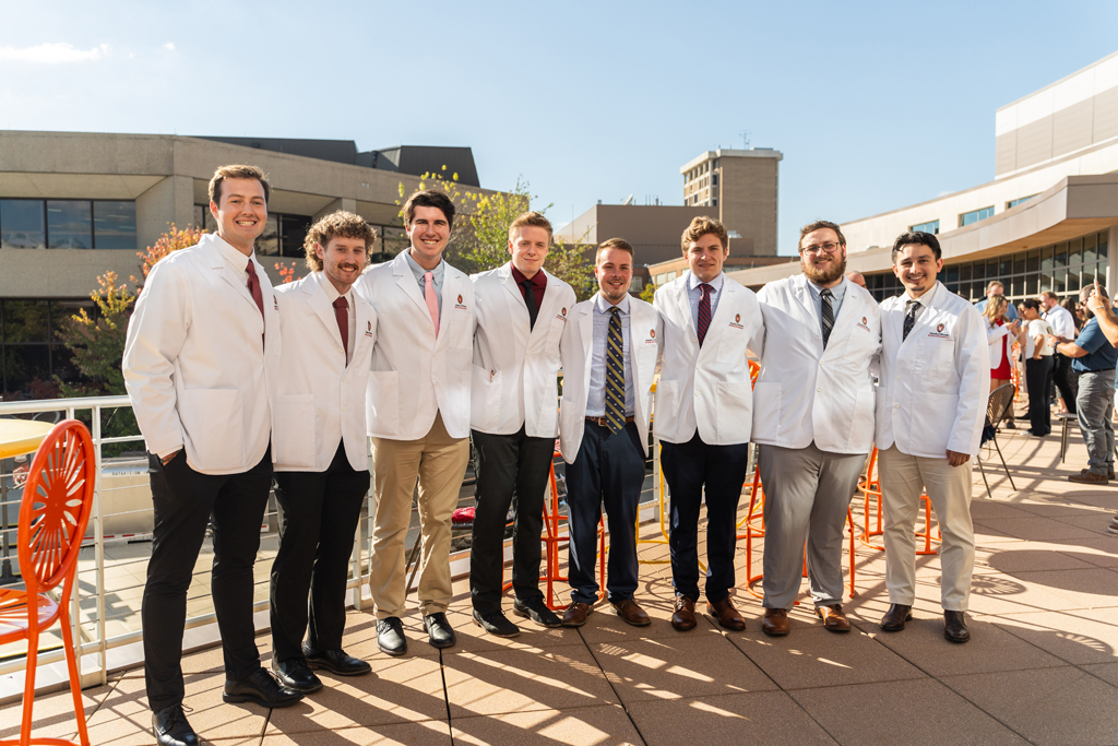 2024 White Coat Ceremony A large group of eight male students pose and smile for a photo outside