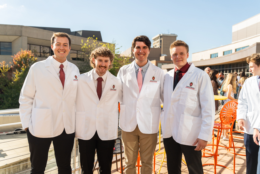 Photo by Paulius Musteikis Four male students in white coats pose for a photo outside