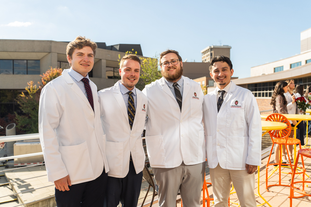 Photo by Paulius Musteikis Four male students in white coats pose for a photo outside