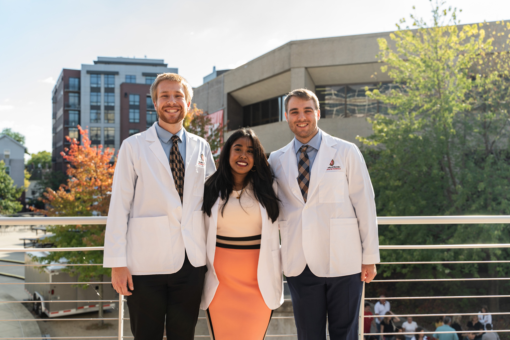 Photo by Paulius Musteikis Three students in white coats pose for a photo outside