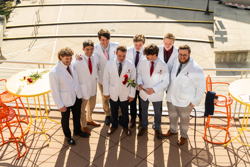 Photo by Paulius Musteikis A group of male students in white coats gather for a photo. The photo is taken from above and the students are looking ahead of them toward a different, unseen photographer.