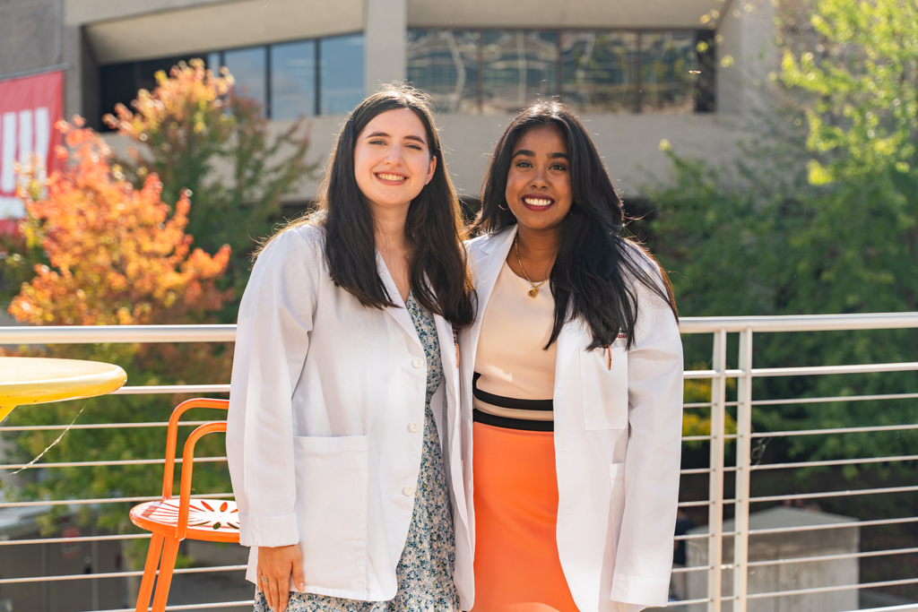 Photo by Paulius Musteikis Two students in white coats smile for a photo outside