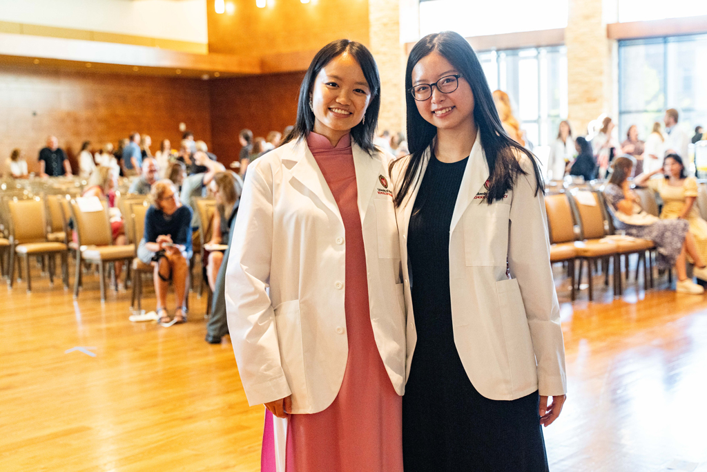 Photo by Paulius Musteikis Two female students in white coats pose in front of audience chairs