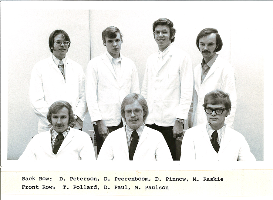 A black-and-white group photo of pharmacy students in white coats.