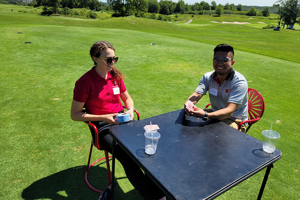 20210813_121610 Check-in people for golfing event sitting at pop-up table in terrace chairs with tickets and cards