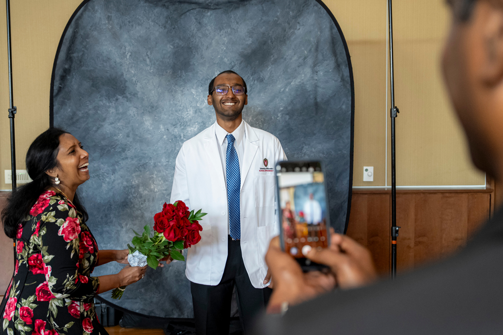 School of Pharmacy White Coat Ceremony Sunday, Sept. 17, 2003. Student posing in white coat with his mom laughing from the side holding roses