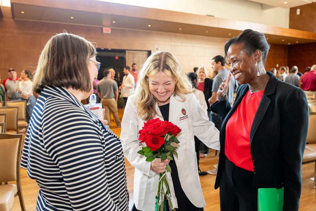 School of Pharmacy White Coat Ceremony Sunday, Sept. 17, 2003. Student in white coat holding roses while laughing with her mother and a staff member