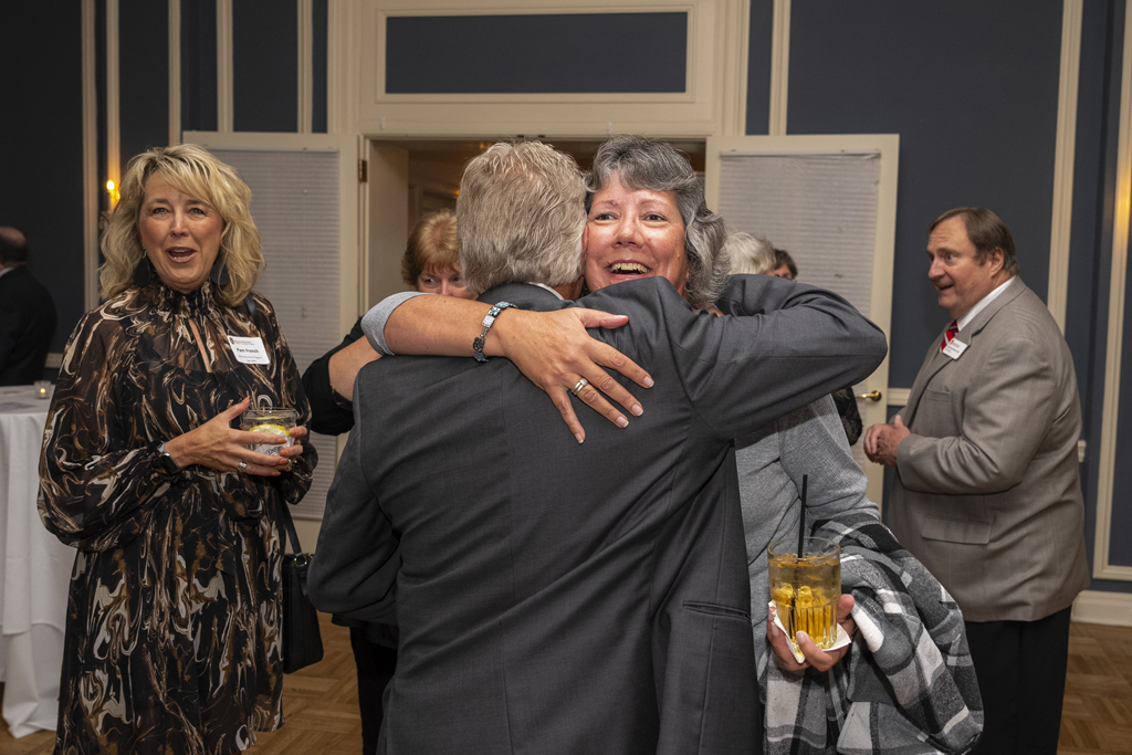 Pamela French smiles in the background while Bob Breslow hugs an attendee