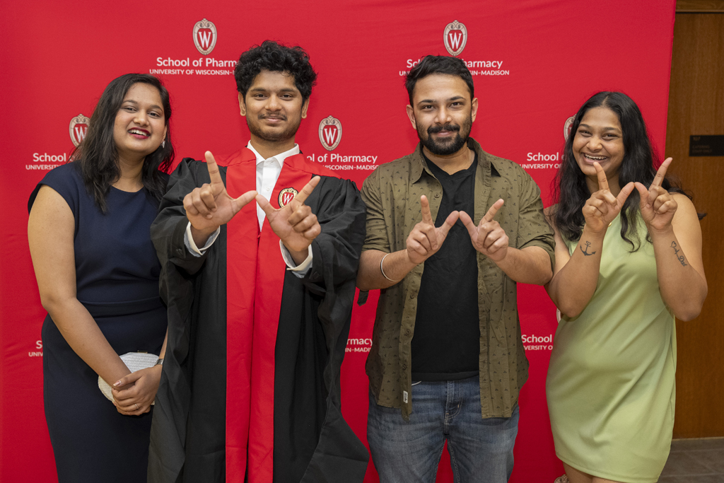 PharmD Graduation Awards Breakfast at the Pyle Center May 10, 2024. A graduate and family members pose in front of a red School of Pharmacy background