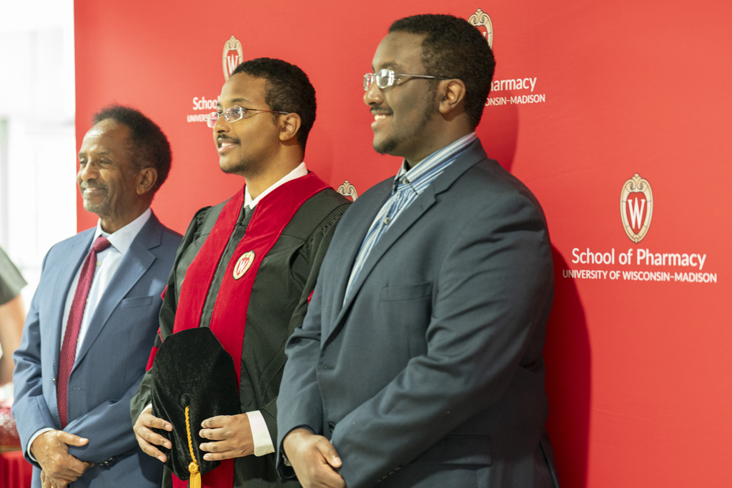 PharmD Graduation Awards Breakfast at the Pyle Center May 10, 2024. A graduate and family members pose in front of a red School of Pharmacy background