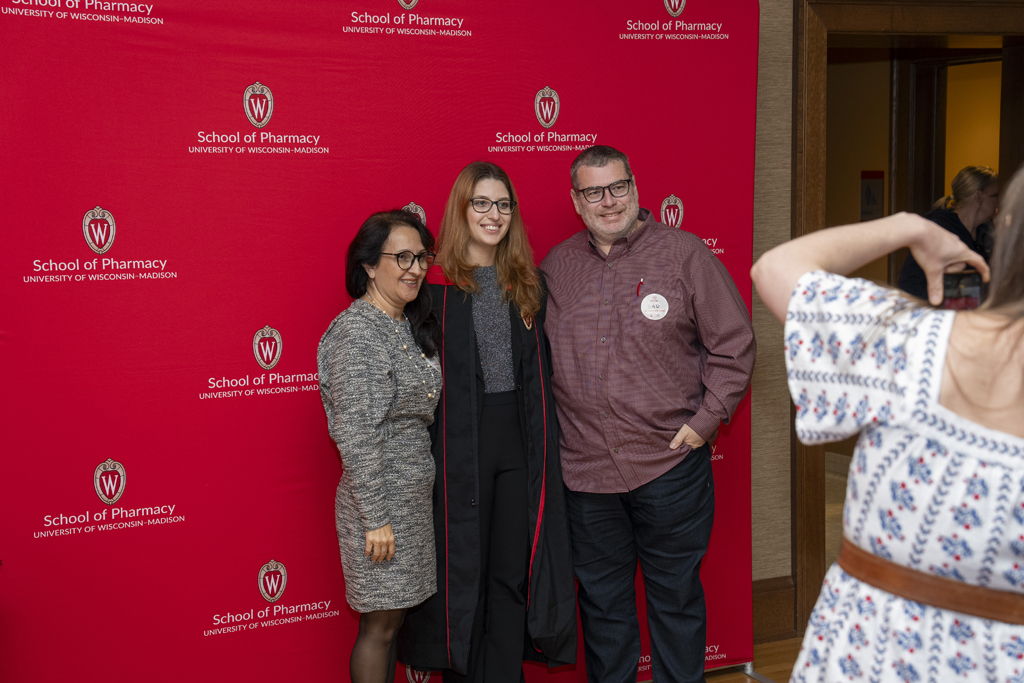 PharmTox Brunch at Carson Gulley May 11, 2024. (Photo © Andy Manis) A graduate poses with his family in front of a red School of Pharmacy background