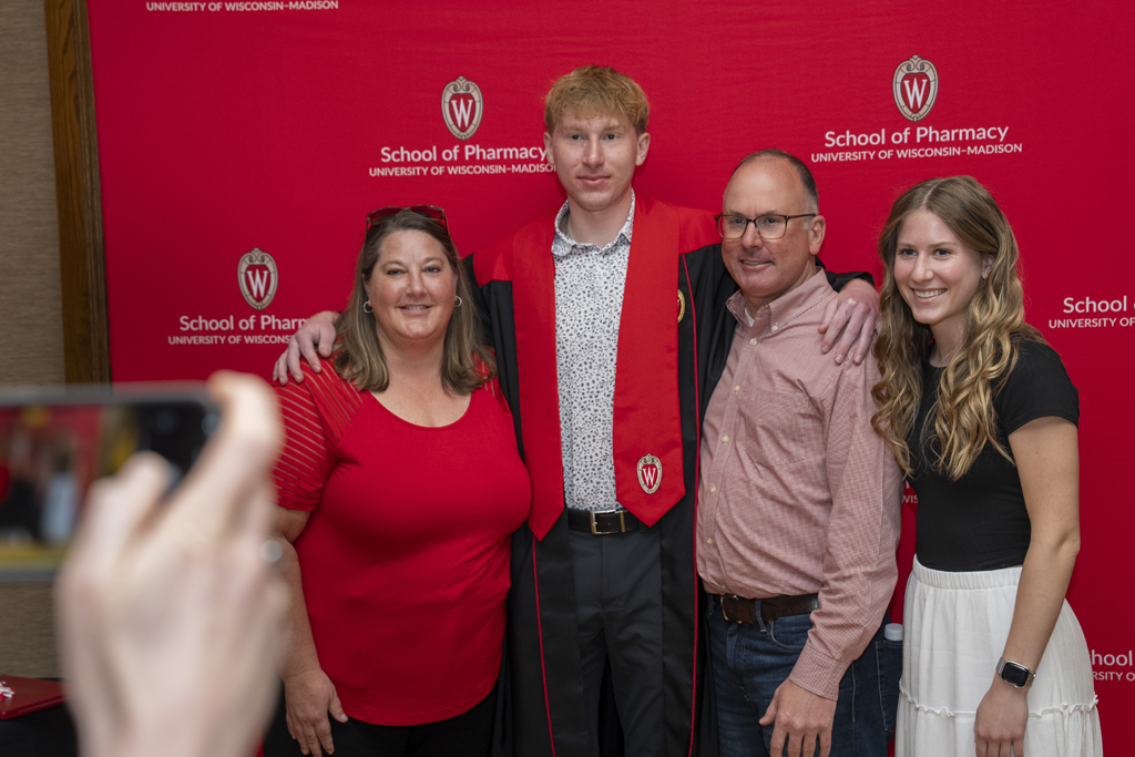 PharmTox Brunch at Carson Gulley May 11, 2024. (Photo © Andy Manis) A graduate poses with his family in front of a red School of Pharmacy background