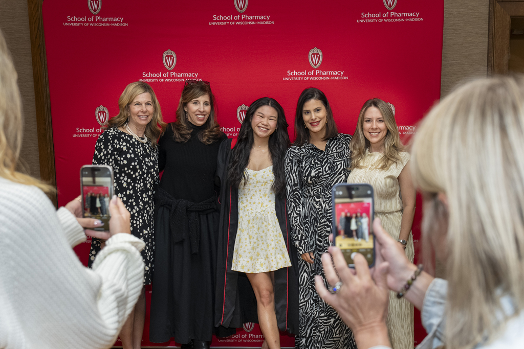 PharmTox Brunch at Carson Gulley May 11, 2024. (Photo © Andy Manis) A graduate poses with family members in front of a red School of Pharmacy background