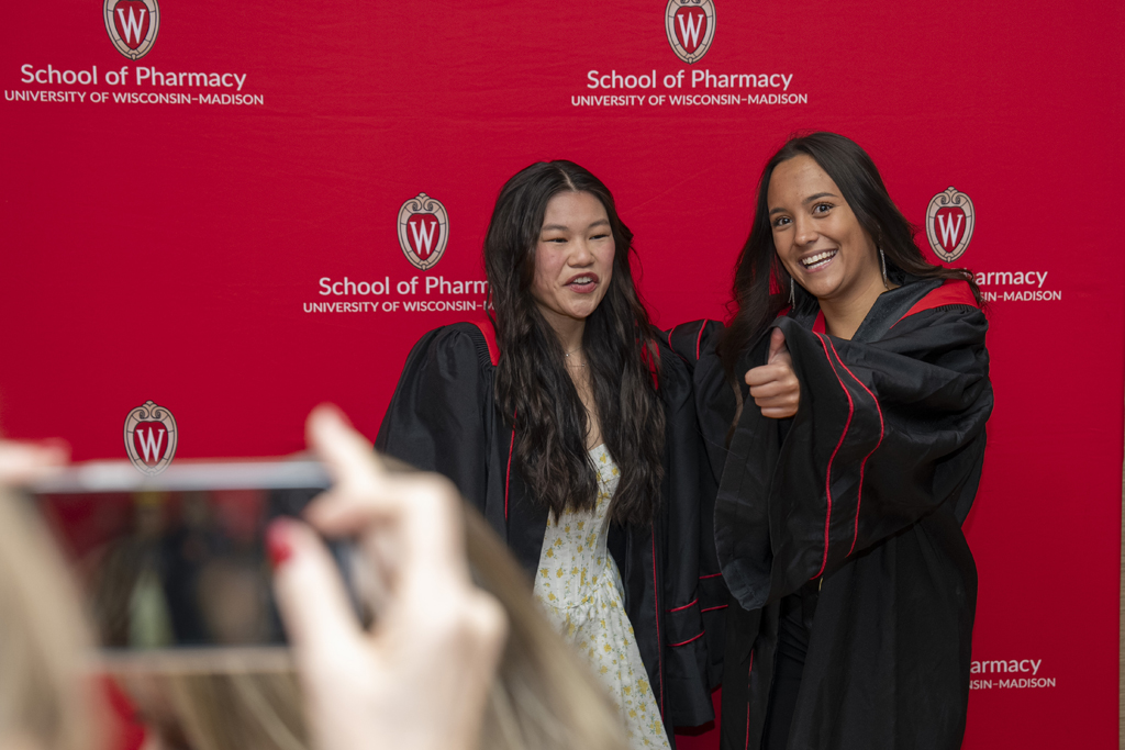 PharmTox Brunch at Carson Gulley May 11, 2024. (Photo © Andy Manis) Two graduates stand by a red School of Pharmacy background