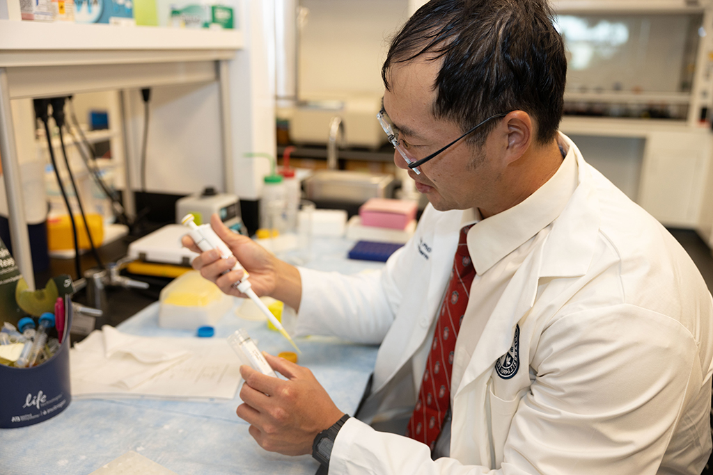 Joe Su works in his lab, holding a small white pipettor