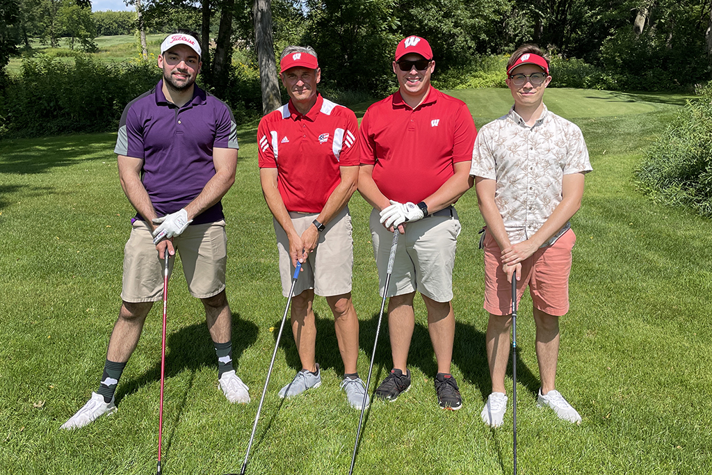 275E7ED3-61FE-446B-8E48-AE24F541E059 A group of alumni smile at the 2022 golf outing, outside in the sun