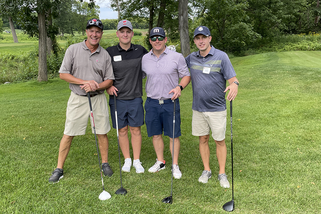 63783697-E83F-4291-AD84-698248D0620F A group of alumni smile at the 2022 golf outing, outside in the sun