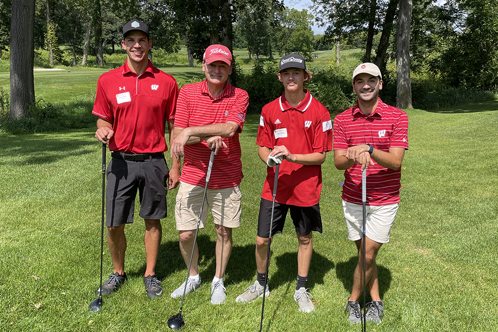 6CDACDD5-AB4E-43F6-88DD-65AC2115467B A group of alumni smile at the 2022 golf outing, outside in the sun