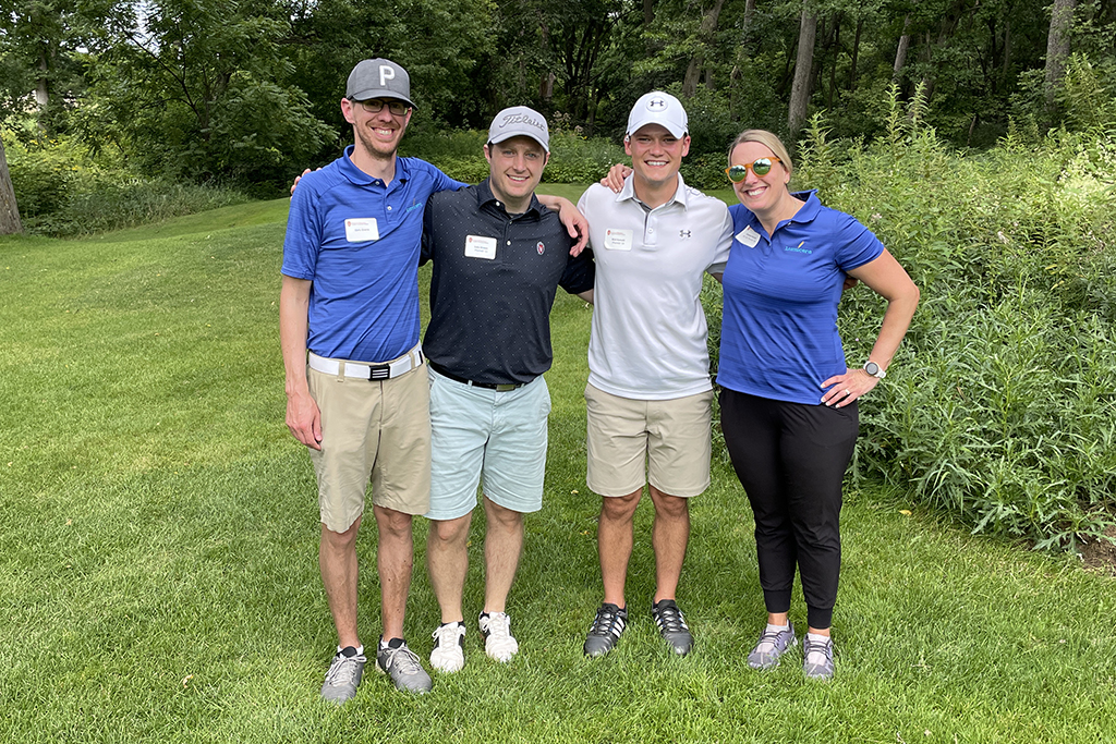 8273363F-047D-44D5-9A6B-6AFEB5D4530D A group of alumni smile at the 2022 golf outing, outside in the sun