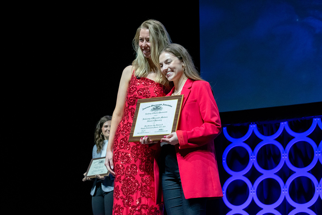 Lauren Glaza accepts an award onstage from a woman in a red dress.