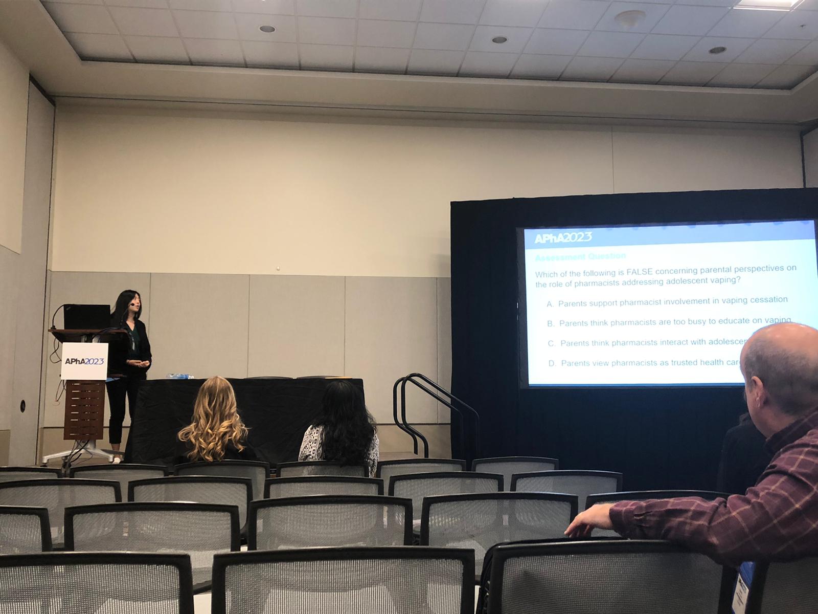 Jenny Li speaks on a stage next to a large screen about her research.