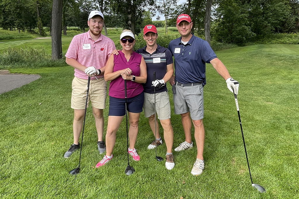 B5B2B851-64FD-4D3C-97EB-1D17CBD98E3D A group of alumni smile at the 2022 golf outing, outside in the sun