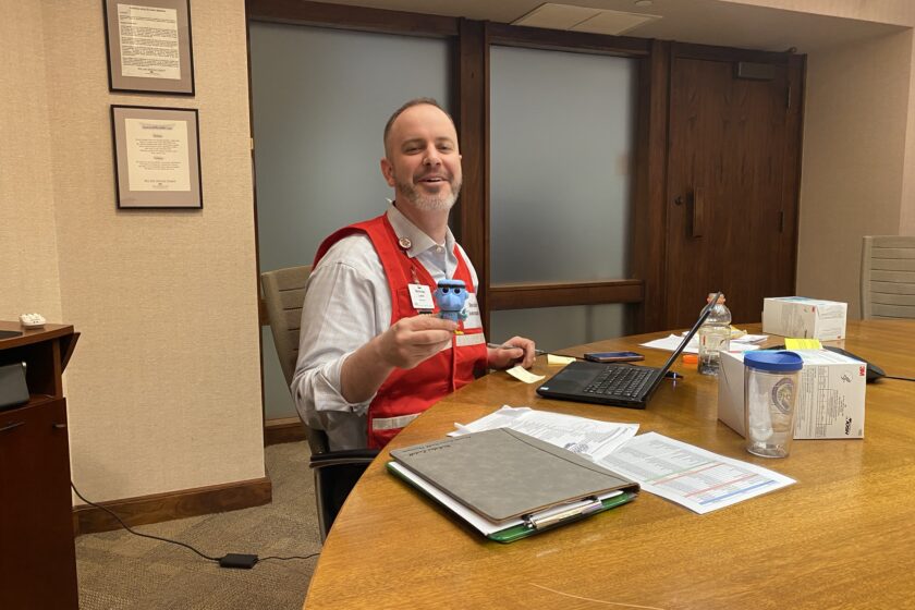 Commander Vest and Spirit Animal - Sam the Eagle Nick Ladell sitting at a table with a laptop in front of him and holding a "Sam the Eagle" character