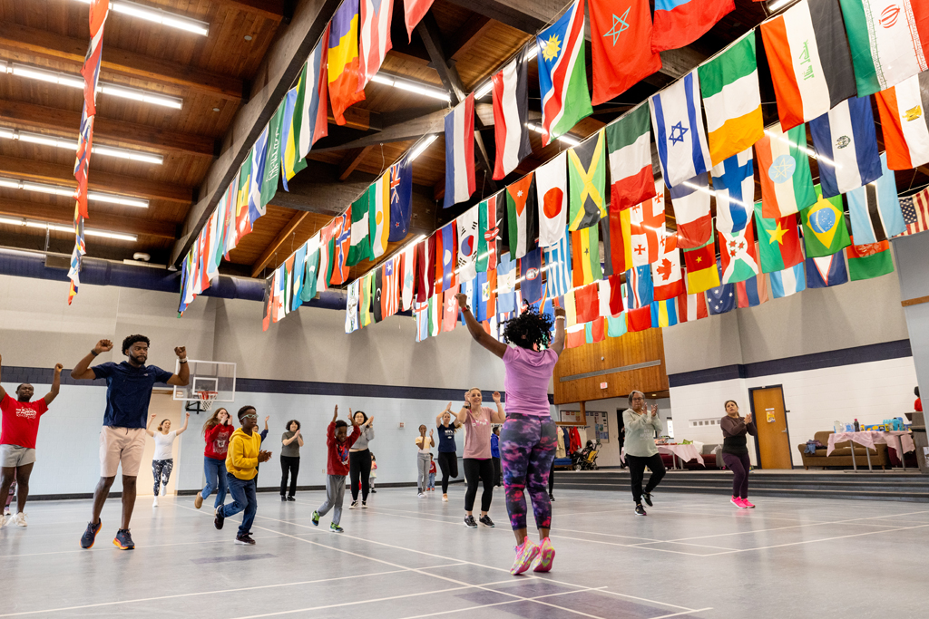 Olufunmilola Abraham jumps in front of a group of all ages in a gymnasium to teach a movement.