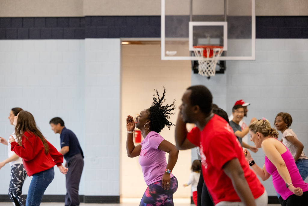 Olufunmilola Abraham dances in front of a group of all ages in a gymnasium to teach a movement.