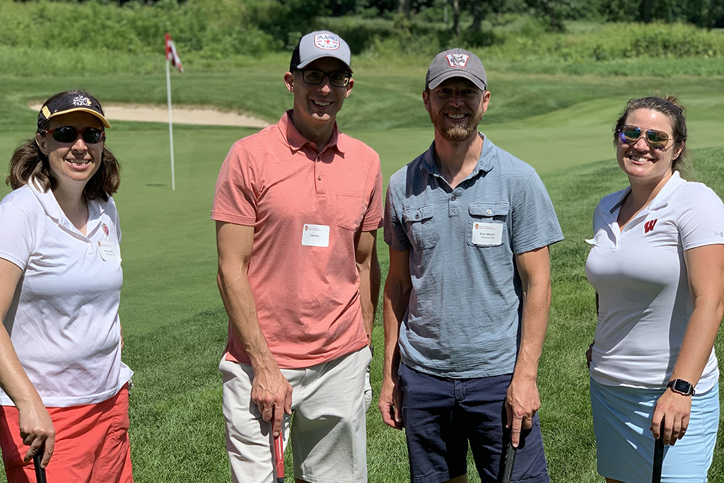 IMG_0117 A group of alumni smile at the 2022 golf outing, outside in the sun