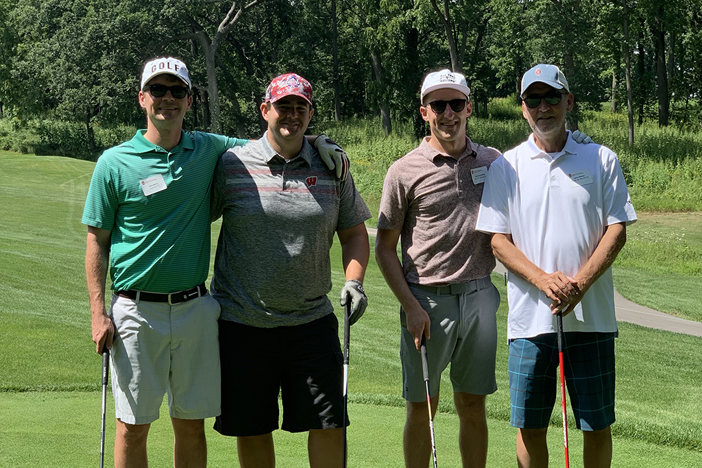 IMG_0169 A group of alumni smile at the 2022 golf outing, outside in the sun