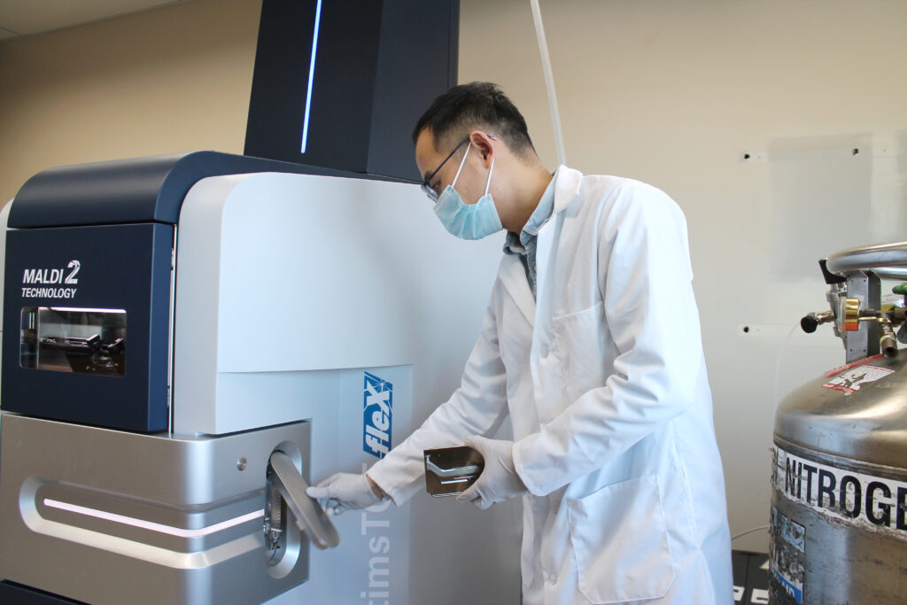 Postdoctoral fellow Hua Zhang is loading the MALDI-2 instrument with a sample plate containing a thin slice of brain tissue from a mouse model of Alzheimer’s disease.